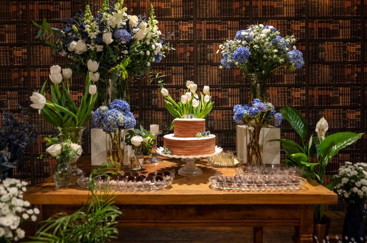 Mesa de doces com flores azuis e estantes ao fundo
