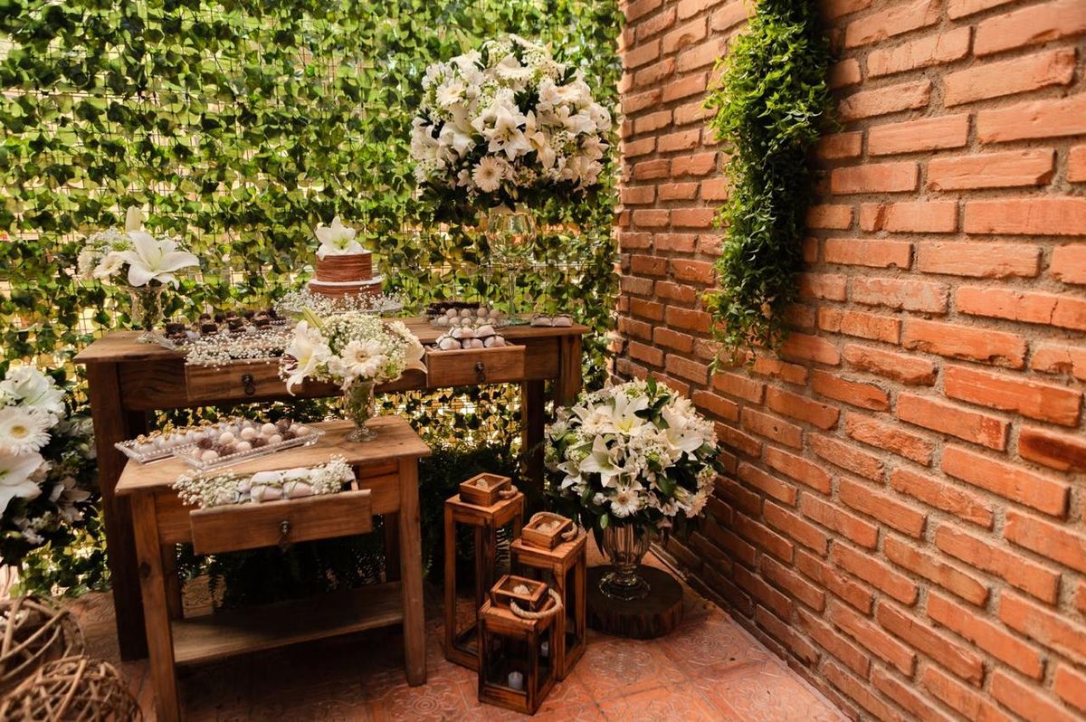 Mesa de doces rústica com flores brancas e parede de tijolos